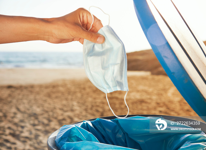 man throws used mask to the trash can on the beach