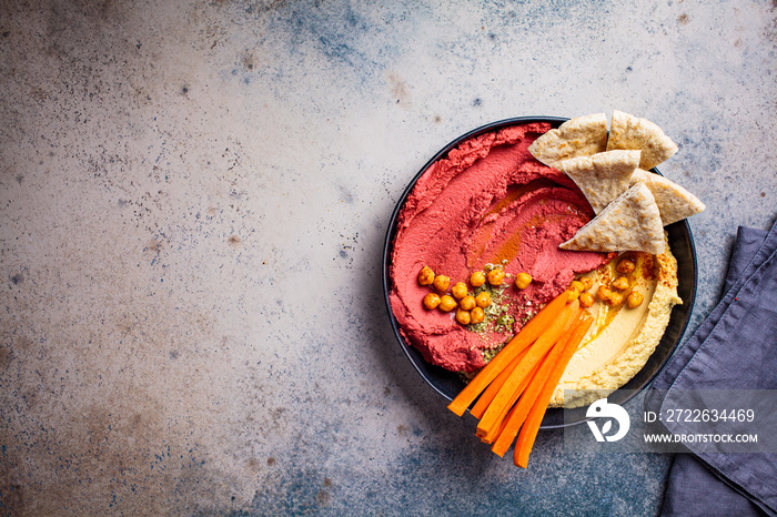 Beetroot hummus and classic hummus in black dish with carrots and pita bread, top view. Plant based diet concept.
