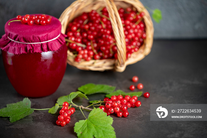 Fresh red currants in a basket and a jar of red currant jam on a dark background