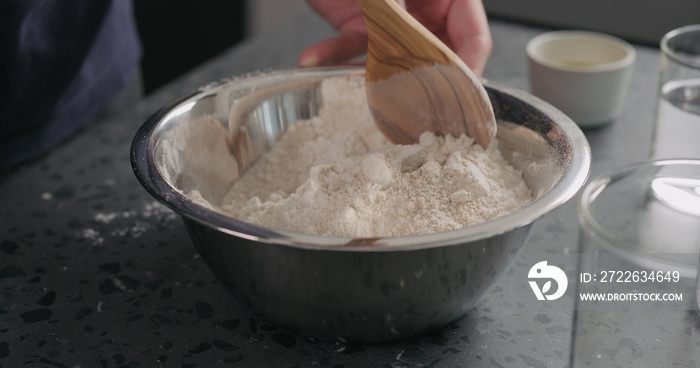 man mixing dry ingredients with flour in steel bowl on concrete countertop