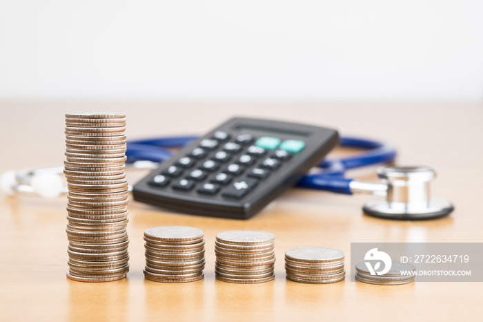 STACKED US QUARTER COINS WITH BLUR BLACK CALCULATOR AND BLUE STETHOSCOPE IN BACKGROUND (MEDICATION CONCEPT)