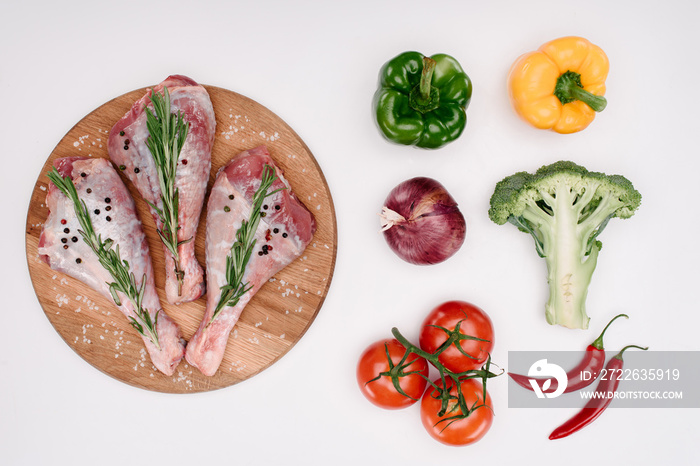 top view of raw turkey legs with rosemary on cutting board with different vegetables near, isolated on white