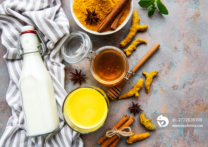 Yellow turmeric latte drink. Golden milk with cinnamon, turmeric, ginger  and honey over concrete background.