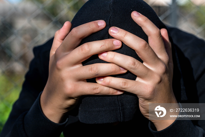 Young unidentifiable teenage boy  holding hes head at the correctional institute , conceptual image of juvenile delinquency, focus on the boys hand.