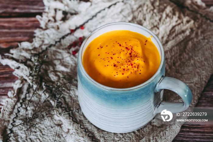 Soupe de courge et carottes aux baies roses dans un bol sur une table de cuisine en bois