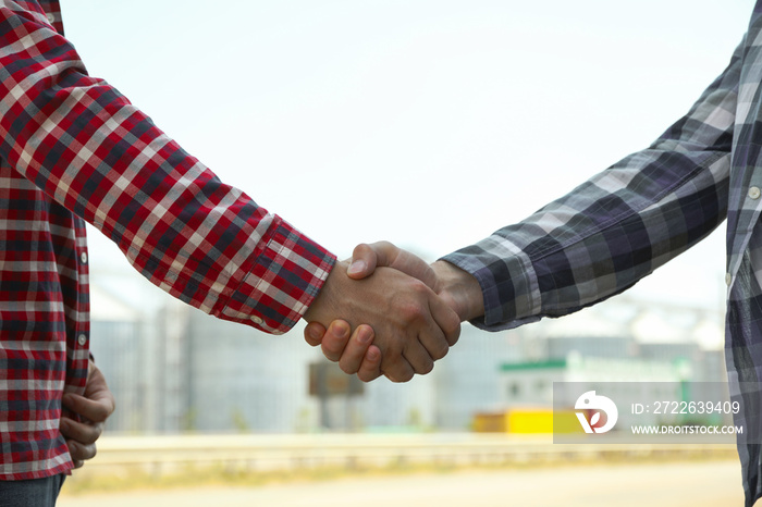 Businessmen shake hands against silos. Agriculture business