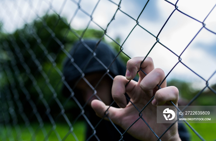 Young unidentifiable teenage boy holding the wired garden at the correctional institute, conceptual image of juvenile delinquency, focus on the boys hand.