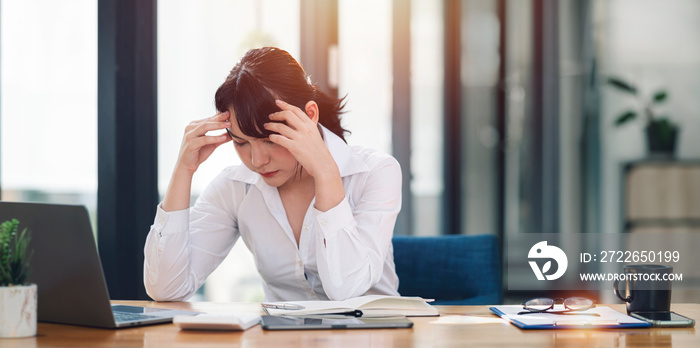 Young Asian businesswoman working on laptop computer, stressed has a headache and thinks hard from work at the office.