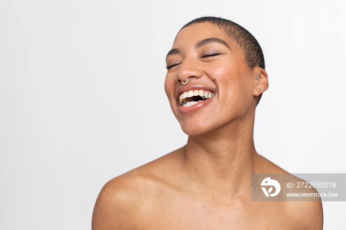 Studio portrait of woman with short hair and nose ring laughing with eyes closed