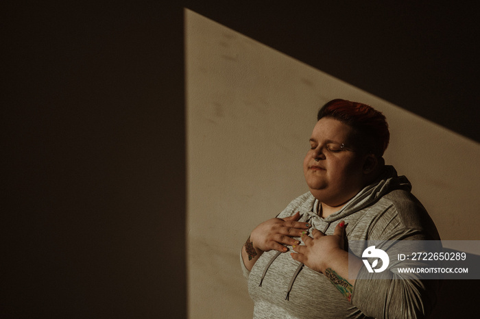 portrait of a plus size person in triangle of light with hands on chest