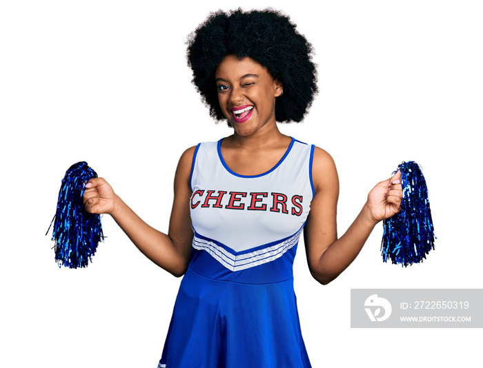 Young african american woman wearing cheerleader uniform using pompom winking looking at the camera with sexy expression, cheerful and happy face.