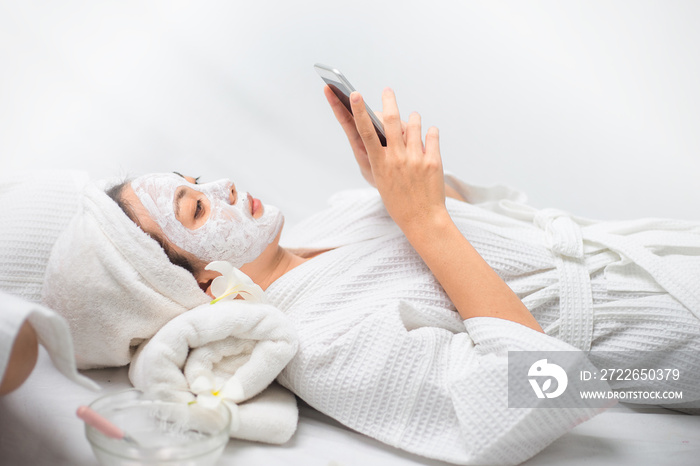 Young Asian women cosmetologist applying mask on face in spa salon and she use mobile phone for chat with her friend.