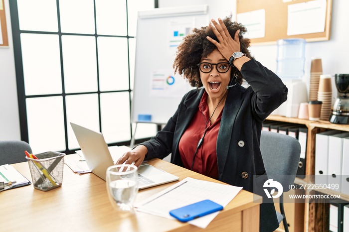 African american woman with afro hair working at the office wearing operator headset surprised with hand on head for mistake, remember error. forgot, bad memory concept.