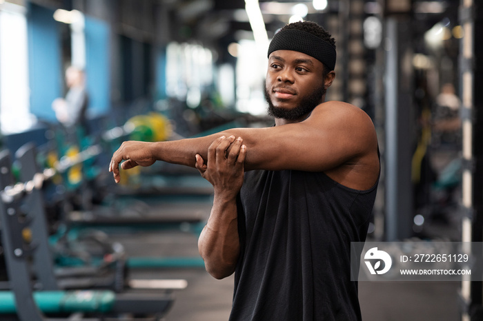 Sportsman black guy stretching his muscles before workout at gym