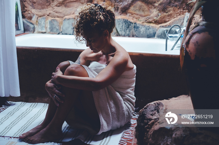 Adult woman sitting on the floor in bathroom at home after abuse or depression disease. Stressed female people sad indoor on the ground. Lady hugging her knees alone