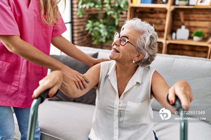 Senior grey-haired woman patient supported for nurse and walker at geriatric