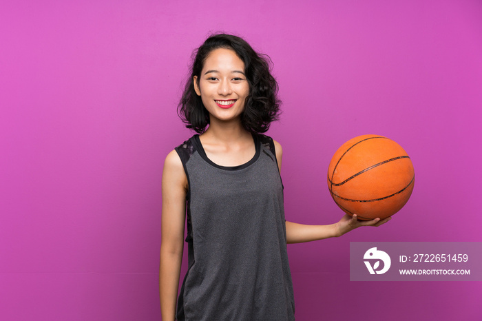 Young Asian woman playing basketball over isolated purple background