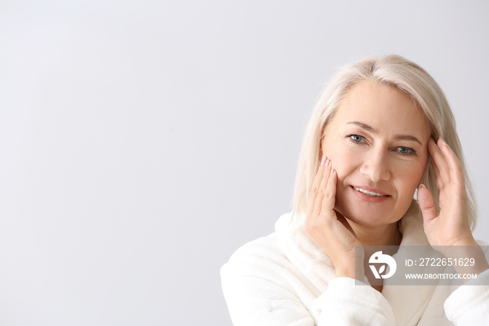 Mature woman giving herself face massage on light background