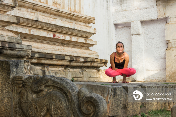 Yogi woman in kukkutasana pose with pink leggings in Srirangapatna temple, Karnataka, India. Yoga instructor practices in Hindu temple