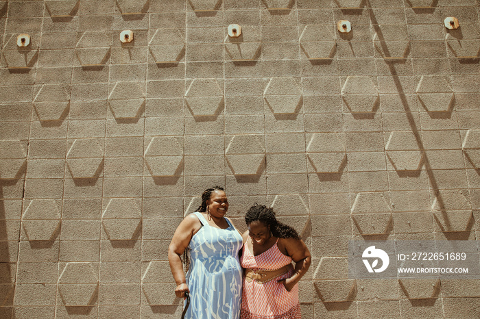 2 plus size African American women stand against a wall laughing