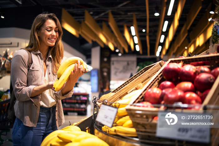 Woman enjoys buying healthy food in supermarket. Customer holding bananas at fruit department.