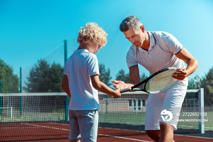 Curly blonde son listening to father while taking tennis racket