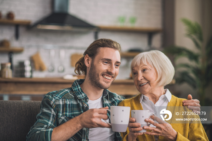 Grey-haired elderly woman having morning coffee with son