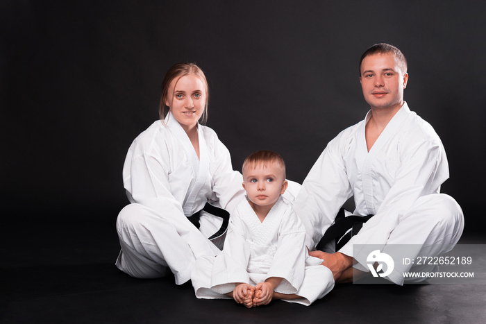 Portrait of happy young family in martial arts uniform standing over black background.