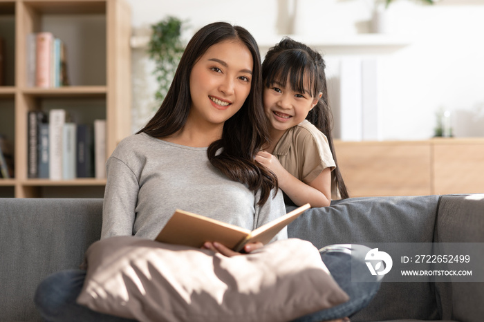 Happy asian young mother smile reading fairy tale story with daughter in living room at home. Little girl enjoy with fairy tale story from mom on couch looking book together.Relaxed time at home