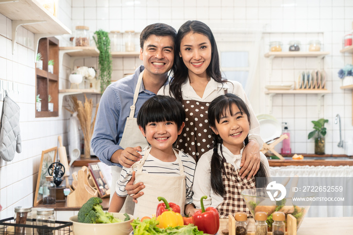 Lovely cute Asian family making food in kitchen at home. Portrait of smiling mother, dad and children standing at cooking counter that food ingredient put on table. Happy family activity together.