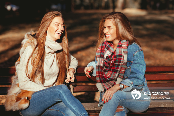 Two young women sitting on a bench in the park and laughing