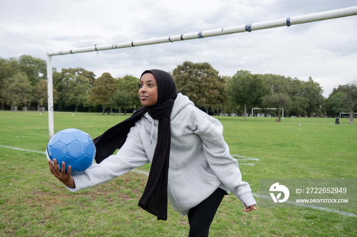 Smiling woman in hijab playing soccer in park