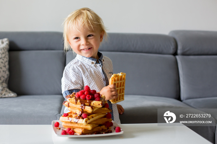 Sweet toddler birthday boy, eating belgian waffle with raspberries and chocolate