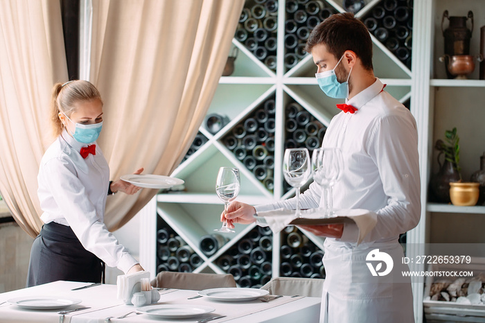 A waiter in a medical protective mask serves a table in the restaurant. Employees of a restaurant or hotel in protective masks. The End Of Quarantine.