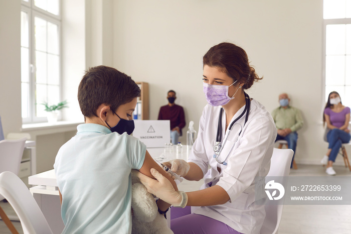 Brave little boy in a face mask looking at the needle while getting a flu vaccine