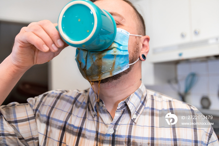 Coronavirus craziness. Close up shot of a man drinking his coffee through a covid protective face mask, making a mess and spilling it over his chest