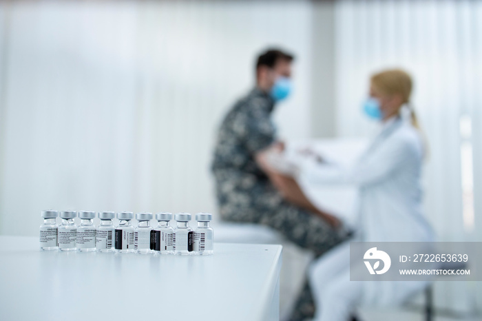 Military vaccination and immunization. Bottles with vaccine and doctor giving injection to the soldier in uniform.