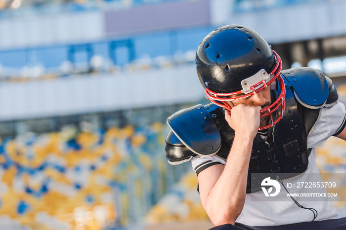 sad young american football player sitting at sports stadium