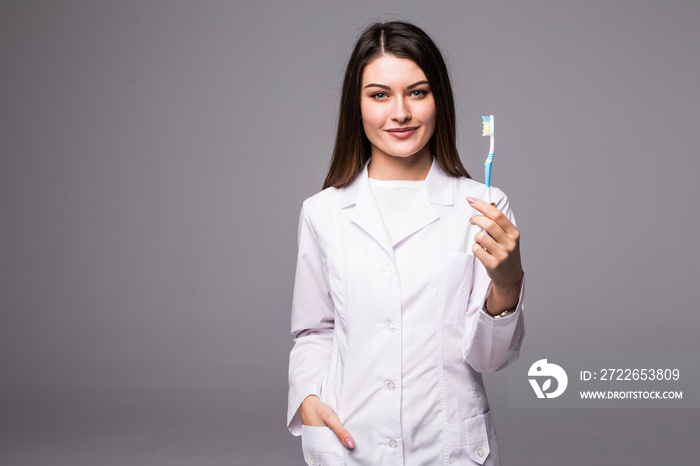 Smiling woman dentist showing tooth brush, isolated over grey background. Young attractive dental clinic assistant brushing.