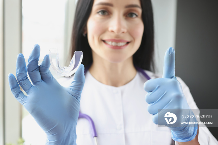 Stomatologist holding mouthguard for teeth and showing thumb up sign