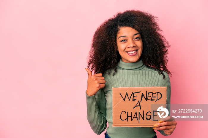 Young african american curly woman holding a we need a change cardboard smiling and raising thumb up