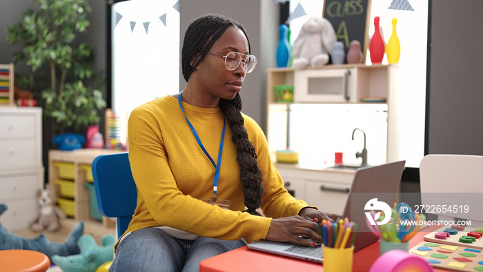 African woman preschool teacher using laptop at kindergarten