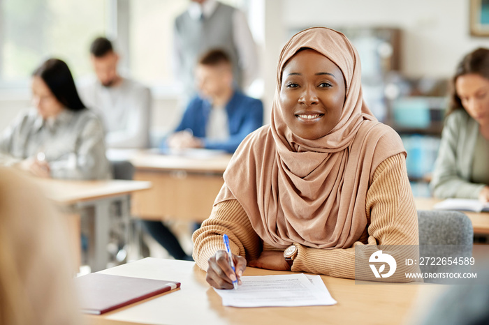 Happy black woman in hijab attending lecture at university classroom.