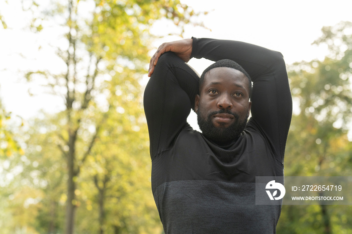 Portrait of athletic man stretching arm in park