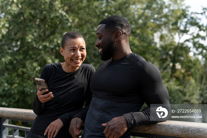 Smiling athletic man and woman holding smart phone in park