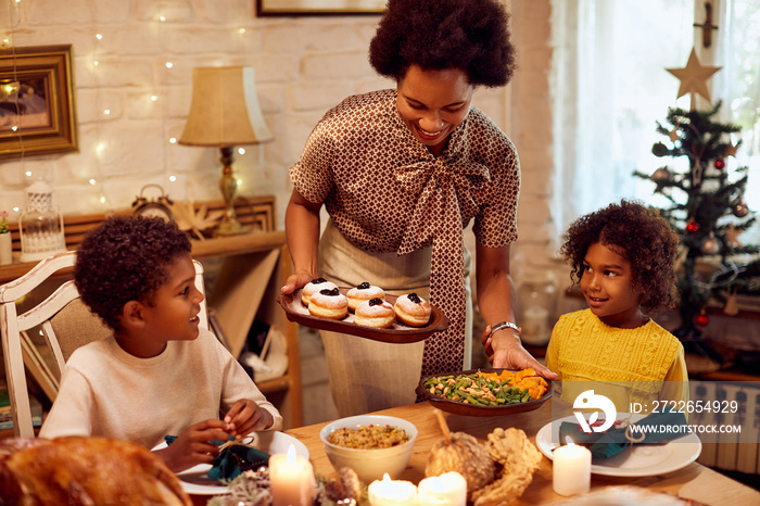 Happy black mother serves food while having Thanksgiving lunch with her children at home.