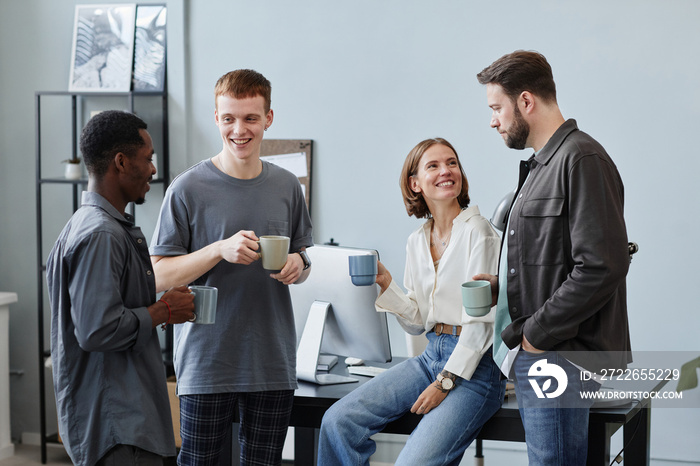 Group of business people drinking coffee from cups and talking to each other during coffee break at office