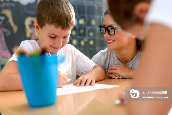 Preschool teacher looking at smart smiling boy at kindergarten