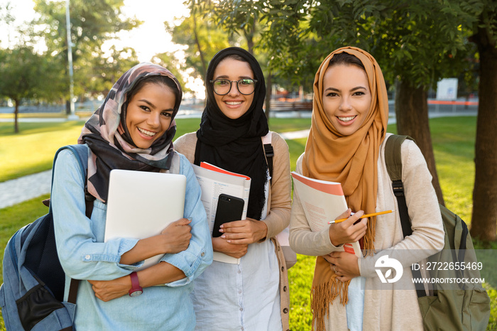 Arabian women students holding books in park outdoors.