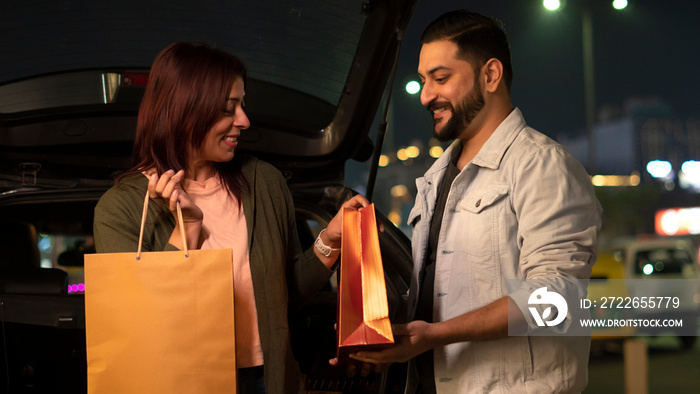 Happy Young Indian Couple shopping at night holding shopping bags